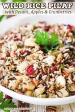 A close-up view of a white serving bowl filled with wild rice pilaf with pecans and cranberries.