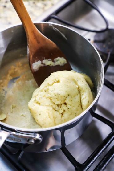 A ball of pastry dough in a medium-sized saucepan with a wooden spoon next to it.