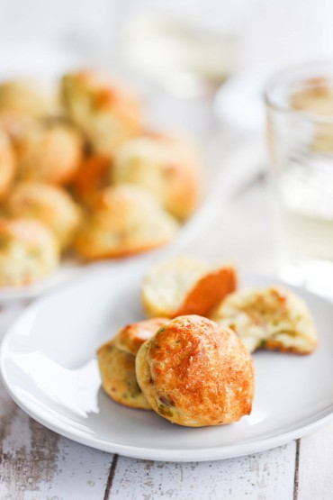 A small white dessert plate holding two parmesan bacon gourgeres next to a plate full of them.