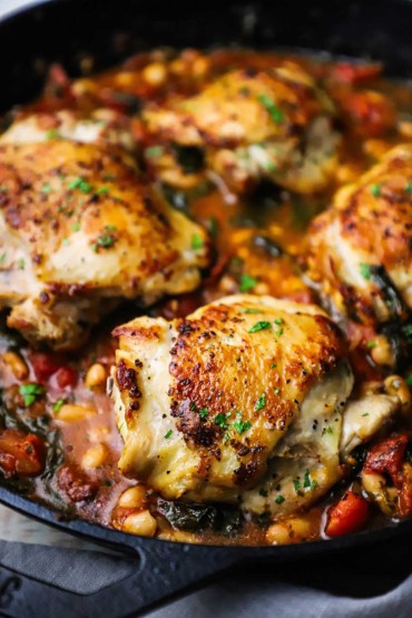 A close-up view of Tuscan chicken with white beans and spinach in a large black cast-iron skillet.