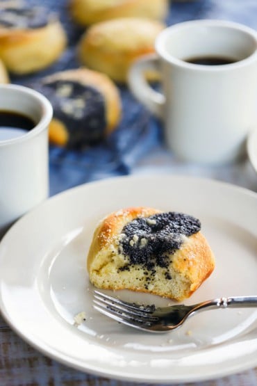 A straight-on view of a half-eaten poppyseed filled kolache on a white dessert plate with a fork next to it.