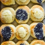 An overhead view of a baking pan filled with freshly baked kolaches topped with poppyseed filling and cream cheese filling.