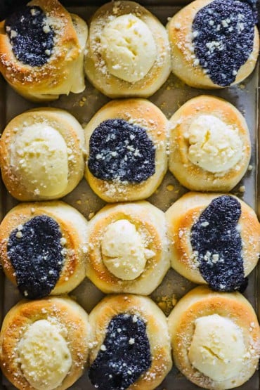 An overhead view of a baking pan filled with freshly baked kolaches topped with poppyseed filling and cream cheese filling.
