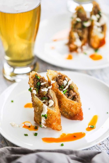 A Philly cheesesteak egg roll that has been cut in half and the two halves are sitting on a white plate upright.