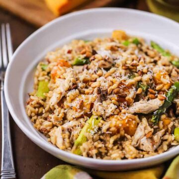 A straight-on view of a shallow white dinner bowl filled with risotto with left-over turkey, roasted butternut squash, and asparagus.