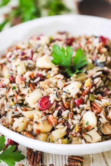 A close-up view of a white serving bowl filled with wild rice pilaf with pecans and cranberries.