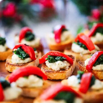 A side view of a platter filled with small toasted crostinis topped with a bean purée, sautéd spinach, and a strip of roasted red bell pepper.