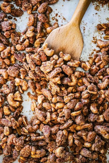 An overhead view of a large baking rack filled with spiced nuts that have a wooden spatula inserted in the middle of them all.
