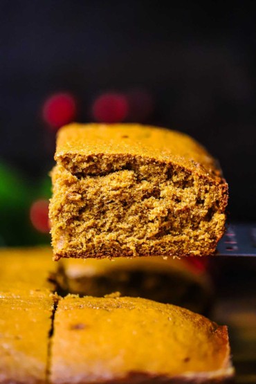 A square piece of gingerbread cake being lifted with a metal spatula from the entire cake.