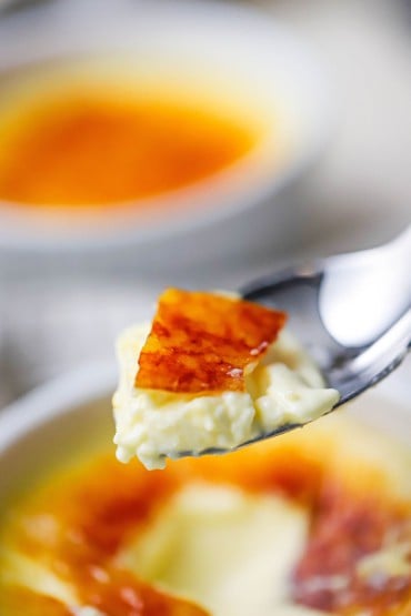 A raised spoon with a serving of crème brûlée on it.