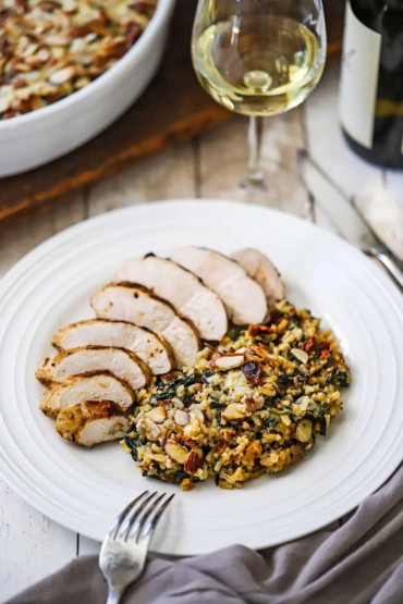An overhead view of a white dinner plate filled with a grilled chicken breast that has been sliced and is sitting next to a helping of wild rice, spinach, and fontina casserole.