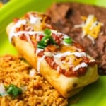 A close-up view of a deep-fried beef chimichanga with a layer of ranchero sauce and melted Colby jack cheese on top.