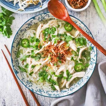 An overhead view of a colorful bowl filled with chicken pho that is garnished with sliced jalapeños, cilantro, and fried shallots.