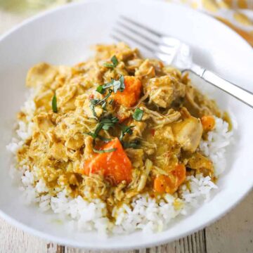 A straight-on view of a white bowl filled with a serving of slow-cooker coconut chicken curry with a glass of white wine nearby.
