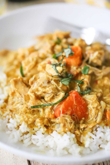A very close-up view of a serving of slow-cooker coconut chicken curry over a bed of steamed white rice all in a white bowl.