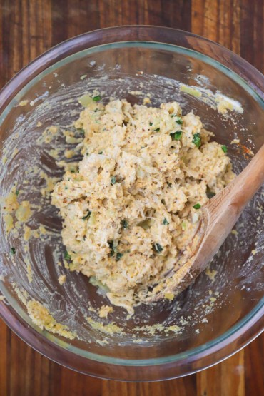 An overhead view of a crab and herbs mixture in a glass bowl with a wooden spoon inserted in the side.