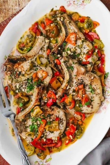 An overhead view of an antique platter filled with four Italian-style smothered pork chops.