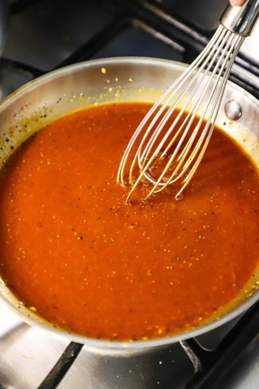 An overhead view of a small skillet filled with homemade BBQ sauce with a metal whisk inserted in the middle of it.