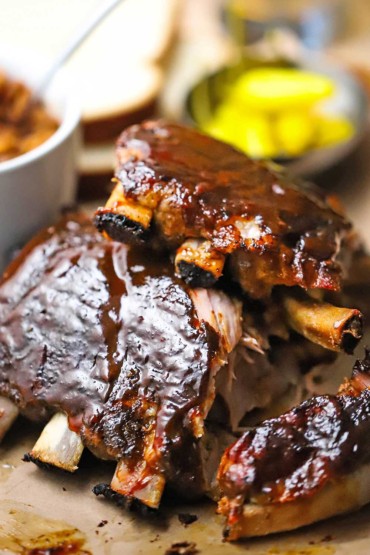 Two half-racks of slow cooker baby back ribs stacked on top of each other and with barbecue sauce smear over the tops of each rack.