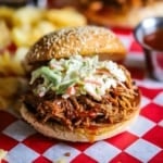 A straight-on view of a slow cooker pulled pork sandwich that is topped with coleslaw and drizzled with Carolina barbecue sauce.