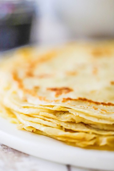 A close-up view of a stack of very thin crepe-like Norwegian pancakes resting on a white circular dish.
