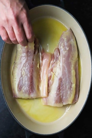 A person dredging two filets of redfish through melted butter in a baking dish.