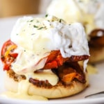 A close-up view of an egg blackstone sitting on a white plate with hollandaise sauce drizzled over the top and on the plate.