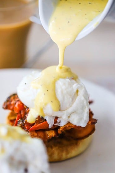 Homemade hollandaise sauce being poured from a small white pitcher over a serving of eggs blackstone.