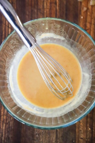 An overhead view of a glass bowl filled with a honey mustard mixture with a whisk in the middle of it.