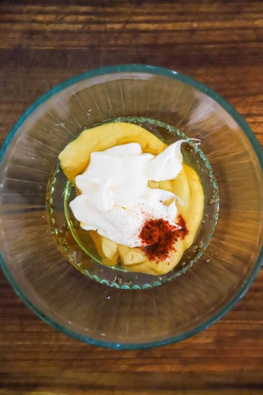 A glass bowl filled with unmixed quantities of mayonnaise, Dijon mustard, honey, and smoked paprika for making a honey mustard dipping sauce.