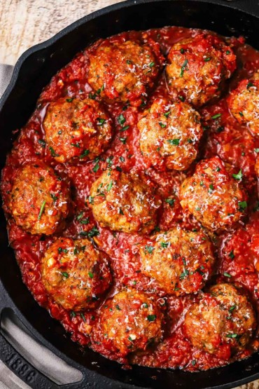 An overhead view of a large cast-iron skillet filled with Italian meatballs resting in a layer of homemade marinara sauce.