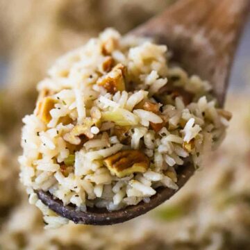 A large wooden spoon holding up a serving of herbed rice pilaf with toasted pecans.