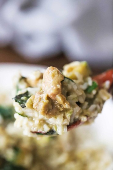 A large wooden spoon being lifted holding a helping of Thai green curry chicken mixed with cooked Jasmine rice.