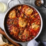 An overhead view of a large silver skillet filled with chicken cacciatore consisting of six seared chicken thighs in a thick tomato sauce.