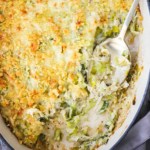 An overhead view of a baking dish filled with a baked leeks gratin with a portion of the casserole missing with a serving spoon in the side.