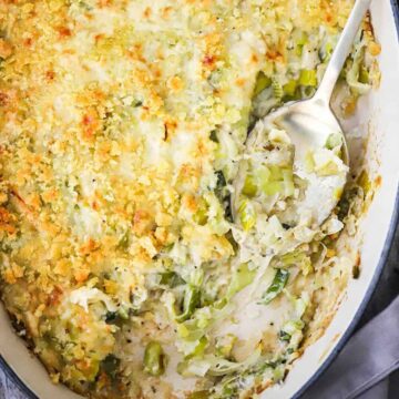An overhead view of a baking dish filled with a baked leeks gratin with a portion of the casserole missing with a serving spoon in the side.