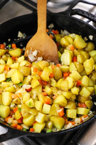 A straight-on view of a skillet filled with cubed yellow potatoes that are being cooked with chopped red bell pepper and jalapeño.