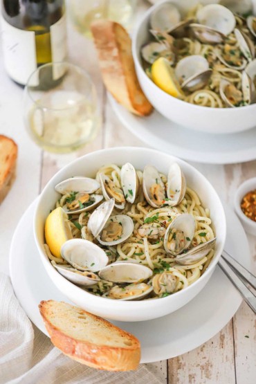 An overhead view of a white pasta bowl filled with a serving of spaghetti alle vongole with clams in their shell sitting on top and piece of toasted bread next to the bowl.