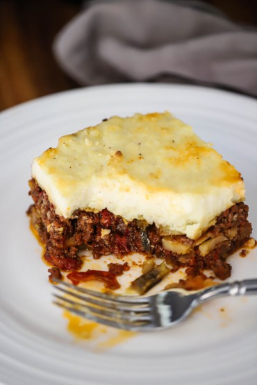 A close-up view of a square slice of moussaka with a bite missing from it.