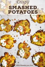 An overhead view of a baking sheet filled with baked smashed potatoes that have been garnished with crumbled bacon, sour cream, and snipped chives.