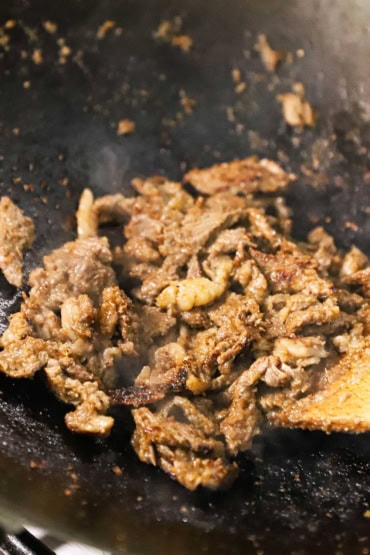A close-up view of strips of beef bulgogi being stir fried in a hot black wok.