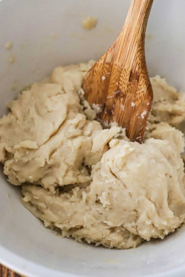 A straight-on view of a ceramic bowl filled with a stiff dough that has a wooden spatula inserted into the middle of it.