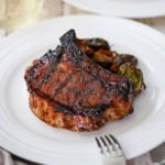 A straight-on view of a grilled balsamic glazed pork chop that is sitting next to a pile of roasted vegetables.