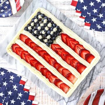 An overhead view of a cake that is decorated with blueberries, sliced strawberries, and vanilla icing to look like an American flag.
