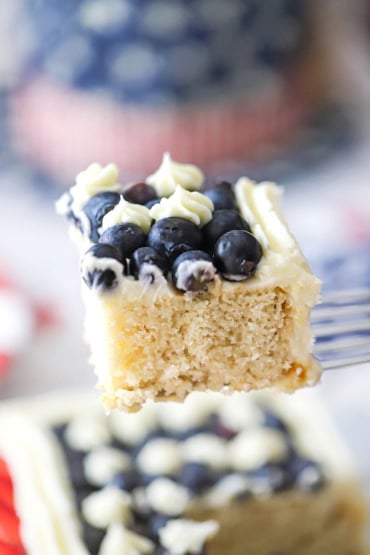 A small metal spatula being used to raise an square piece of an American flag cak that is topped with fresh blueberries and buttercream icing.
