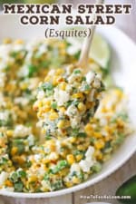 A close-up view of a large serving spoon lifting up a helping of Mexican street corn salad over a bowl filled with the same.