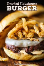 A close-up view of a smoked steakhouse burger that has a pile of fried onion strips sitting on top of melty provolone cheese and the top bun resting off to the side.