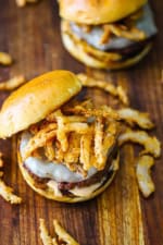 An overhead view of a smoked steakhouse burger sitting on a wooden cutting board with another similar burger in the background.