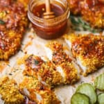 A straight-on view of a cutlet of hot honey chicken that has been cut into strips and drizzled with hot honey sauce and is surrounded by more cutlets and butter pickles.