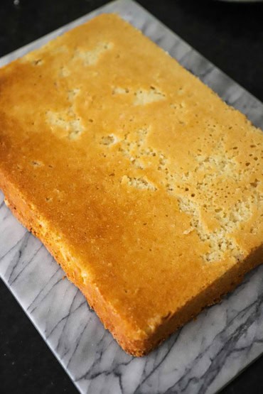 A view from above of a white cake that has been inverted out of the cake pan onto a slab of marbel.